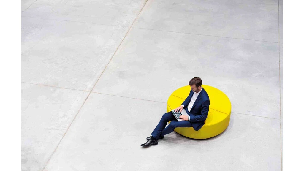 Businessmann sitzt auf einer gelben Sitzgelegenheit auf großen grauen Fliesen