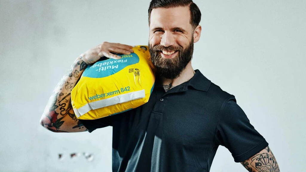 Fliesenleger trägt den Sack des weber.xerm 842 aus der BlueComfort-Produktfamilie über die Schulter