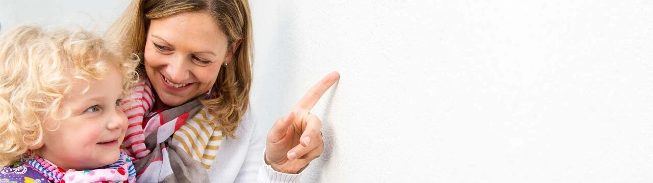Mutter mit Kind im Arm zeigt auf eine Fassade