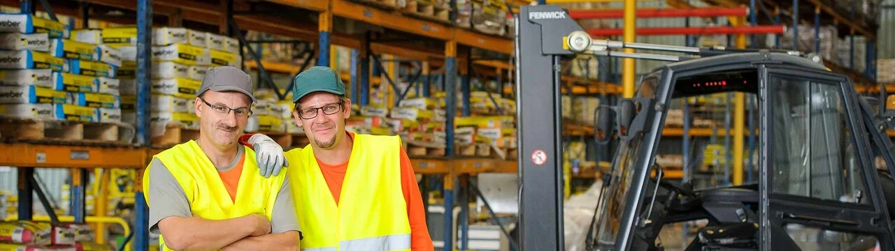 Zwei Männer in gelben Warnwesten stehen vor einem Regal mit Produkten vom Baustoffhersteller Saint-Gobain Weber