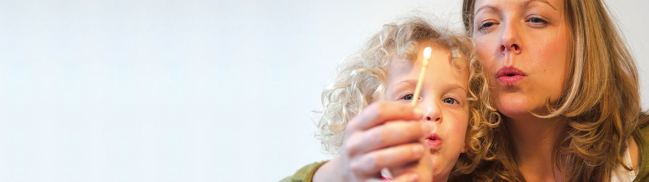 Mutter pustet mit ihrem Kind ein brennendes Streichholz aus