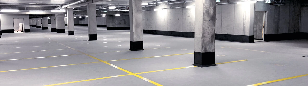 Aufnahme in einer Tiefgarage mit grauem Boden und gelben Parkkennzeichnungen, wo die Sockel der Säulen und Wände mit weber.tec Superflex OS 5b abgedichtet wurden