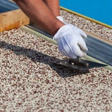 Hand mit Handschuhen drückt Colorquarz in Bodenfläche ein