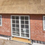 Backsteinhaus mit einem bodentiefen Fenster, wo noch der Sockel abgedichtet werden muss