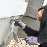 Person trägt Abdichtung auf Sockel mit zweischaliger Bauweise auf