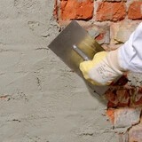 Nahaufnahme, wie ein Wassersperrputz mit einer Kelle auf ein Mauerwerk aufgebracht wird