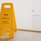 Aufnahme einer Fläche, in die eine frische Spachtelmasse eingebaut worden ist. Im Vordergrund steht ein gelber Aufsteller vor der Fläche mit der Aufschrift Läuft bei mir: Mit Fließspachtel von Saint-Gobain Weber