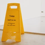 Aufnahme einer Fläche, in die eine frische Spachtelmasse eingebaut worden ist. Im Vordergrund steht ein gelber Aufsteller vor der Fläche mit der Aufschrift Läuft bei mir: Mit Fließspachtel von Saint-Gobain Weber