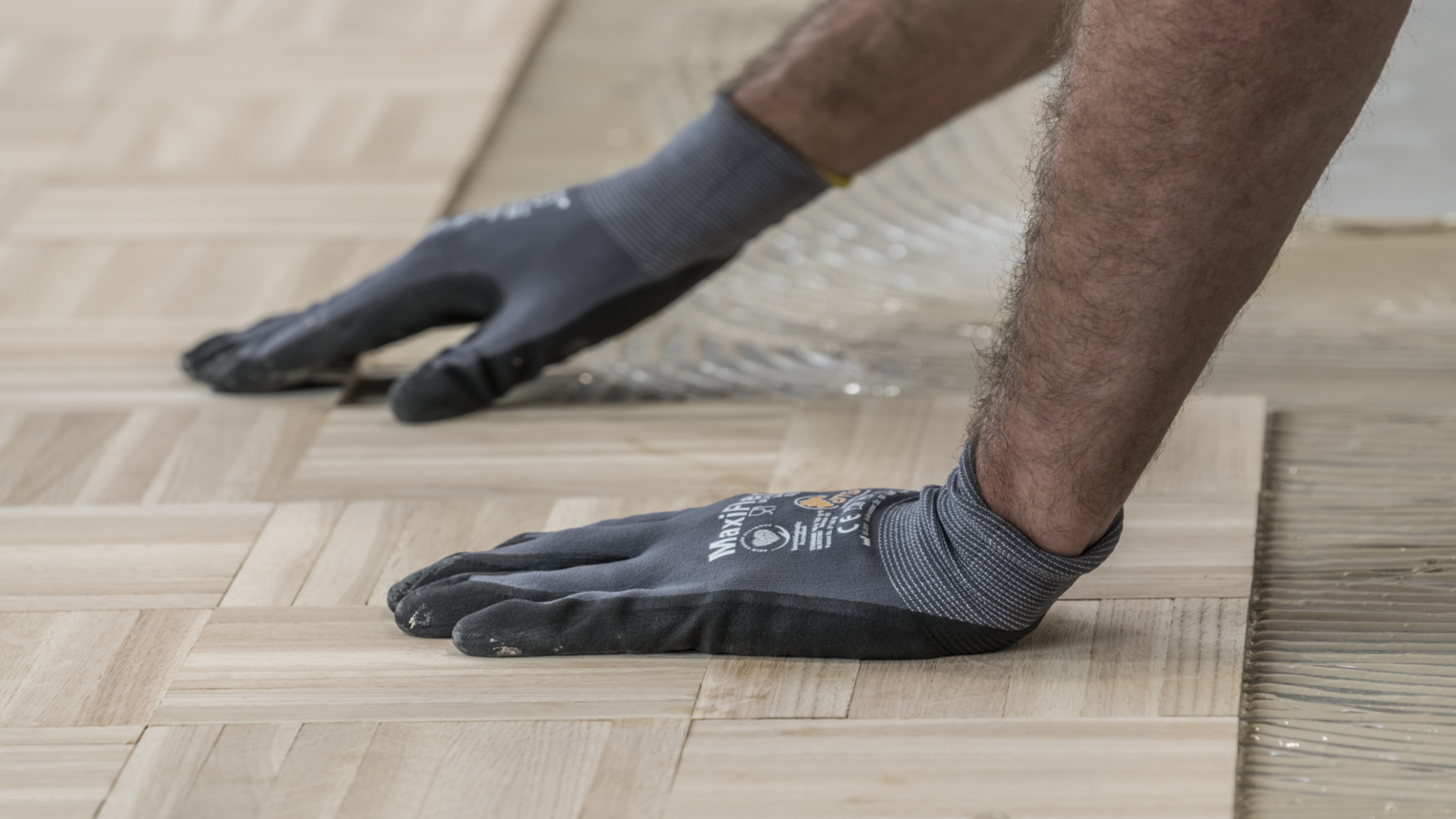 Parkettklebstoff Zwei Hände mit schwarzen Handschuhen verlegen Parkett mit einem Produkt aus dem Weber Klebstoffsortiment