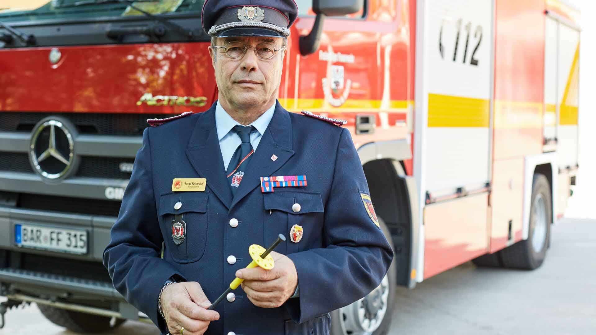 WDVS Dübel Feuerwehrmann in Uniform mit einem WDVS-Dübel in der Hand vor einem Feuerwehrauto