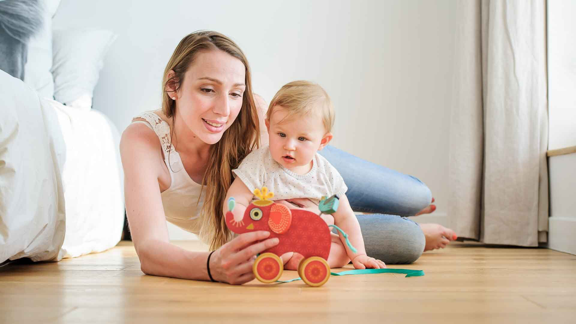 Kalkputz Mutter und Kind spielen auf Holzboden mit einem roten Elefant vor einer weißen Wand