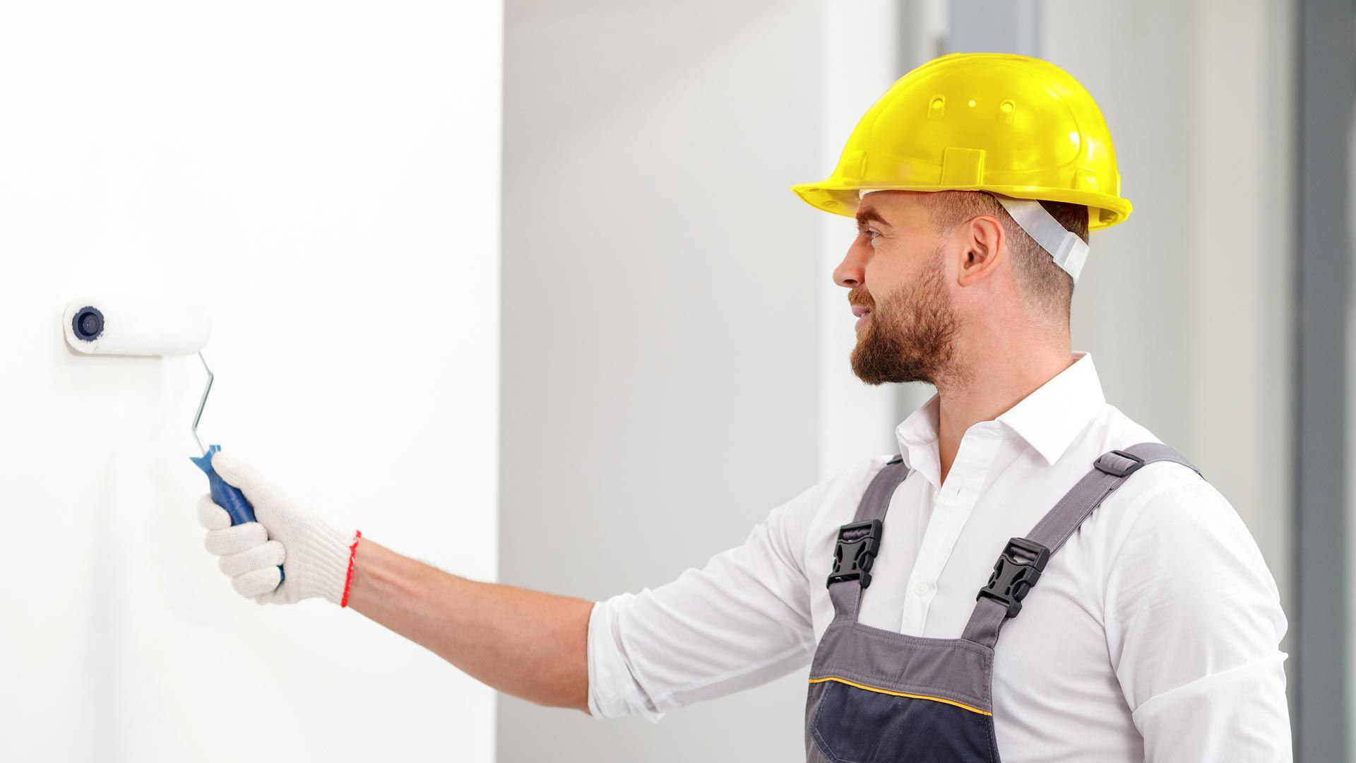 Wandfarbe weber.ton reno Wand wird von einem Handwerker mit gelben Helm in weißer Farbe gestrichen