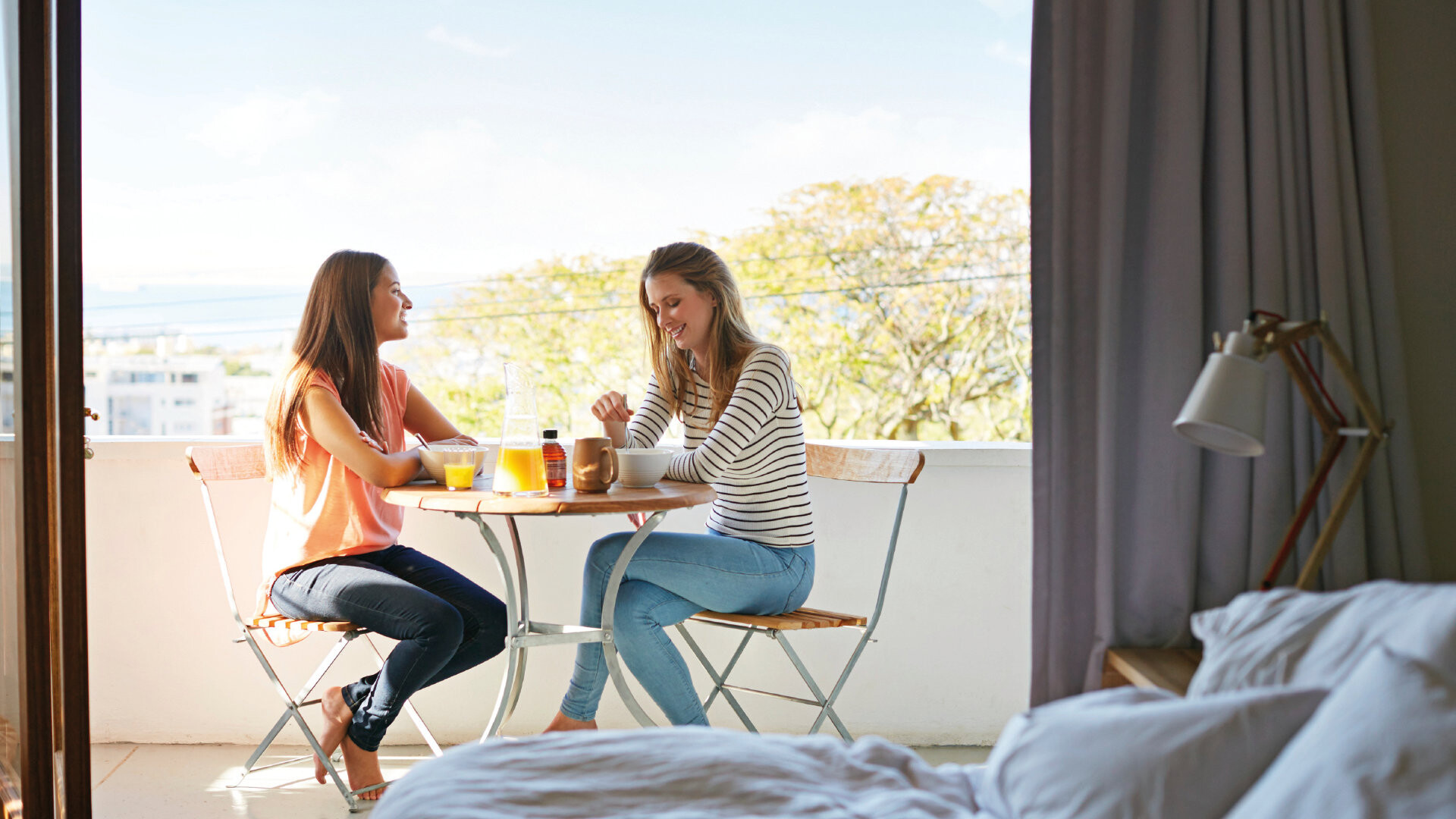 Balkonabdichtung Zwei Frauen sitzen auf dem Balkon an einem Balkontisch beim Frühstück