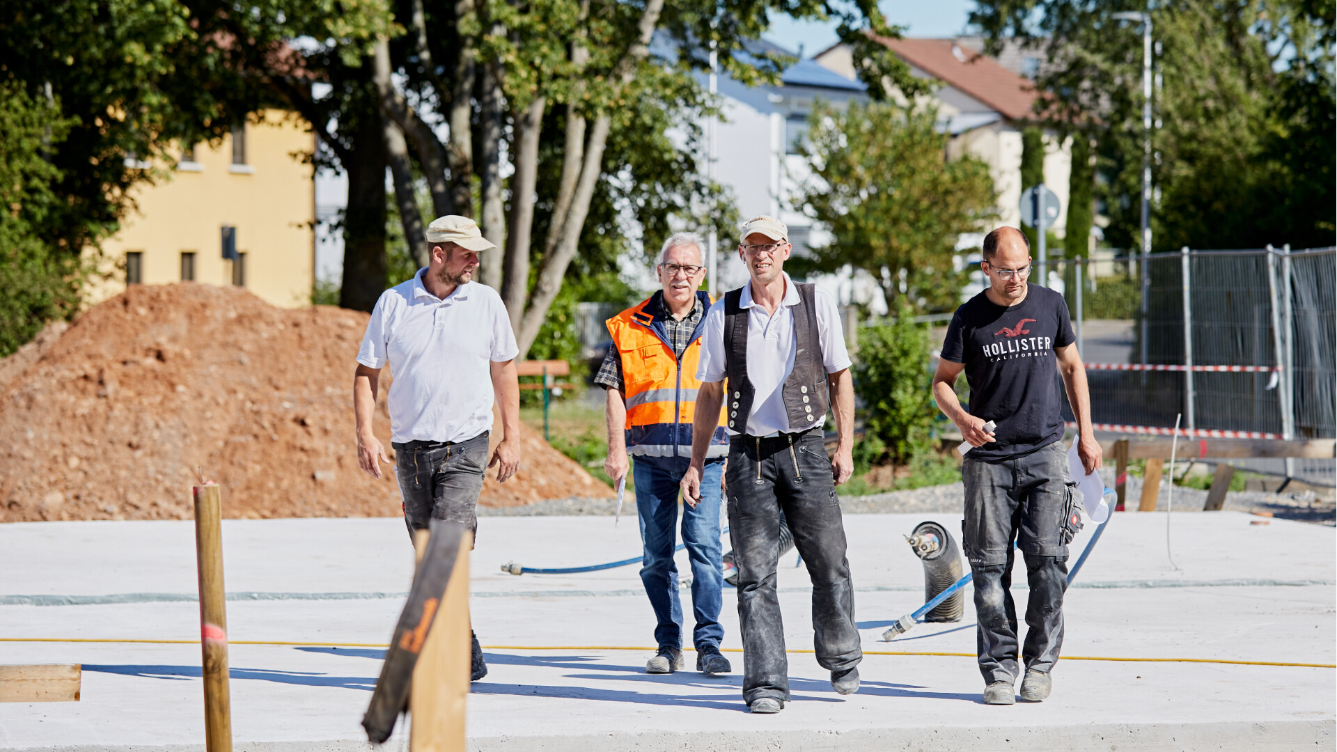 Entspannt auf der Baustelle Vier Fachhandwerker gehen auf einer Baustelle im Sommer entspannt auf die Kamera zu