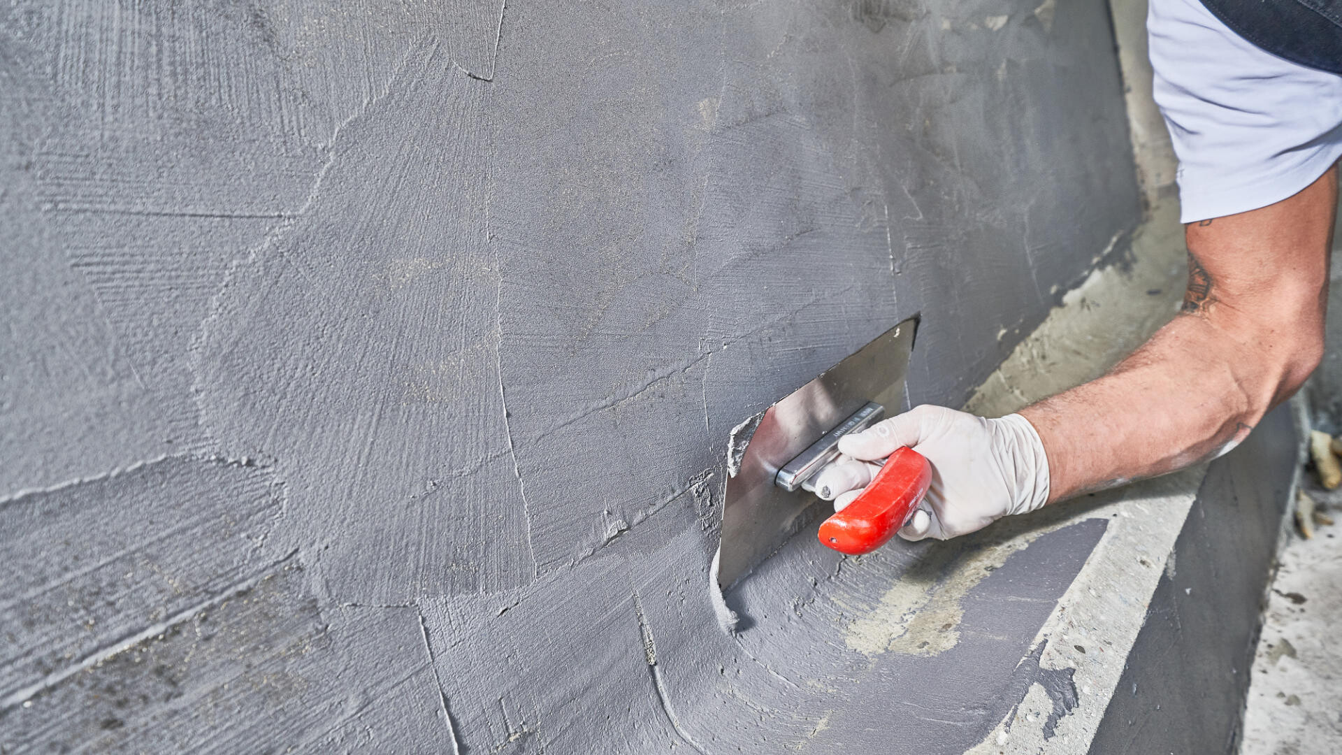 Sockelabdichtung Nahaufnahme wie Handwerker mit einer Kelle eine Sockelabdichtung im Sockelbereich aufzieht