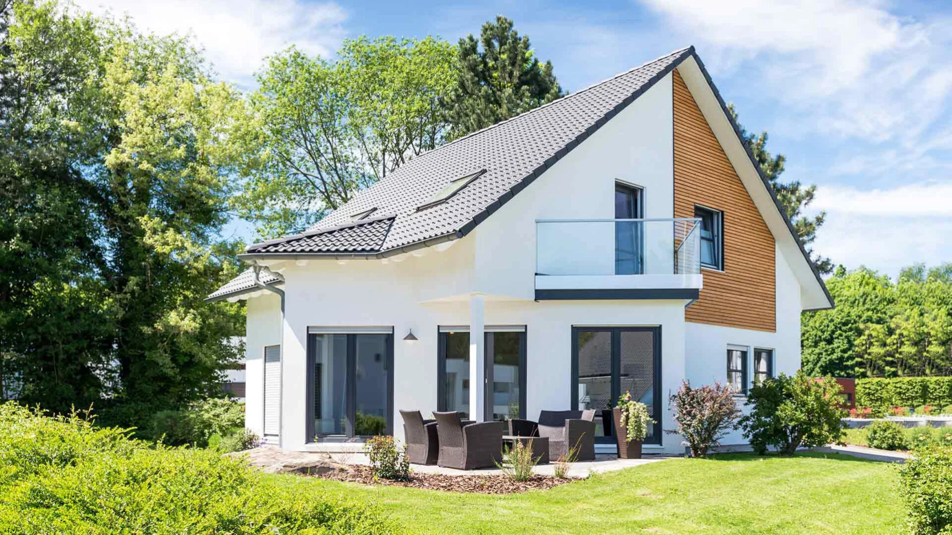 Einfamilienhaus mit einer Fassade aus weißem Putz und hellem Holz in einem grünen Garten