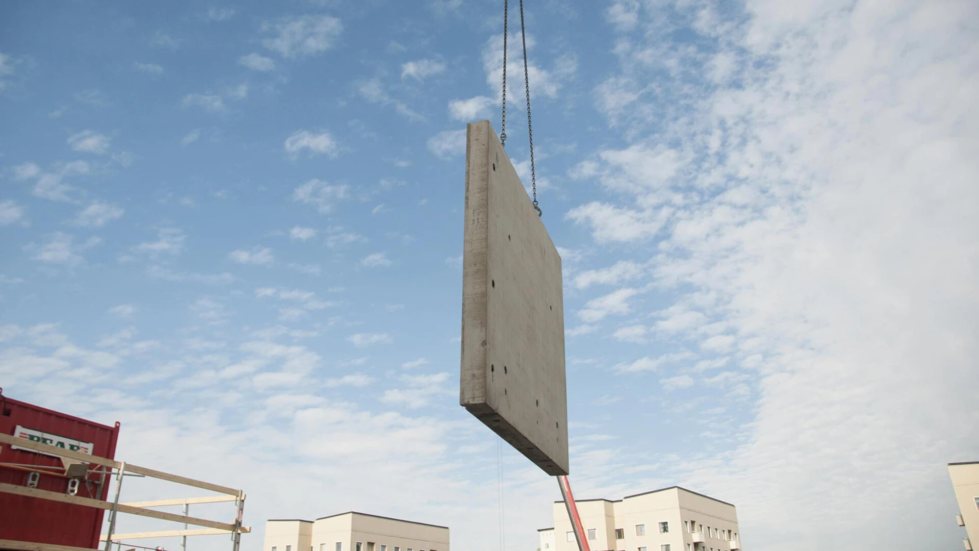 Nahaufnahme einer Präfabrikation einer Gebäudewand vor blauem Himmel, die mit dem Kran an Ihren Platz transportiert wird