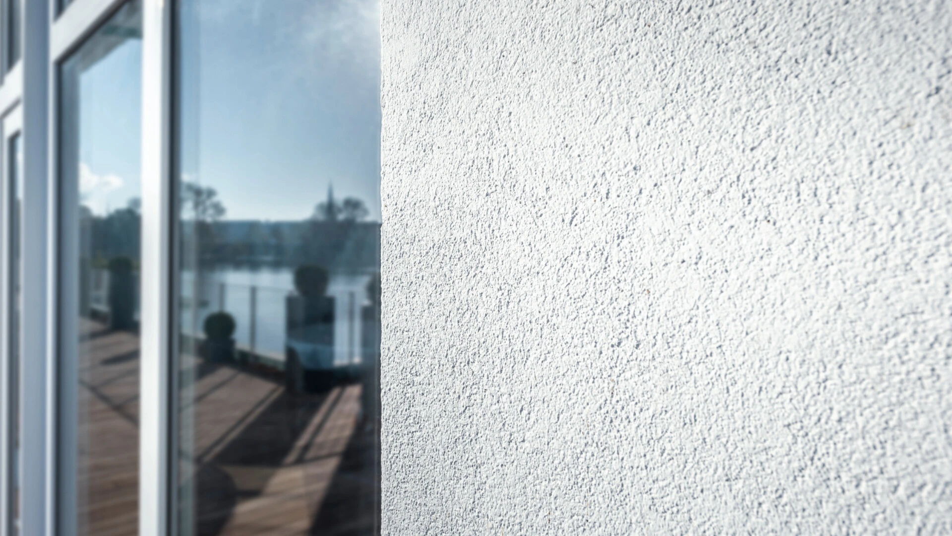 Nahaufnahme einer Fassade, wo man auf der rechten Seite den AquaBalance Putz aus der Nähe sieht und auf der linken Seite ein Fenster, in dem sich Wasser spiegelt
