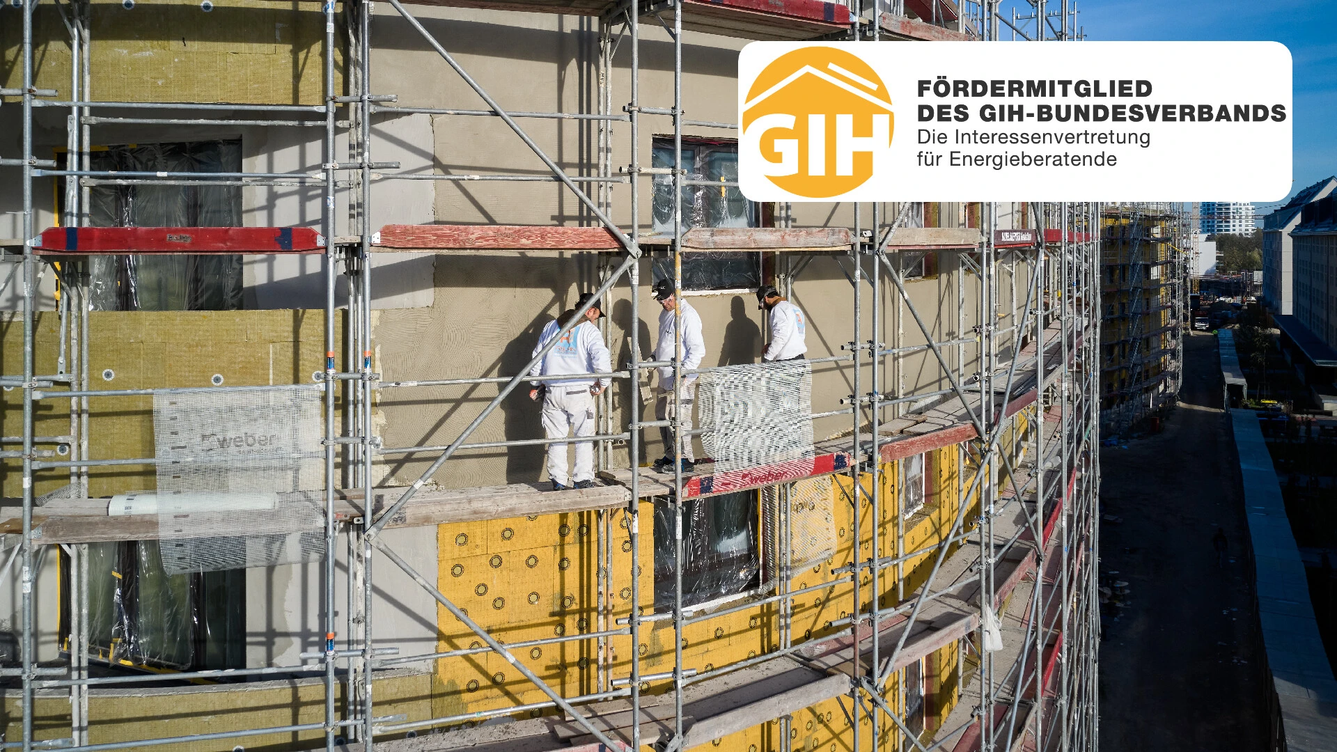 Aufnahme einer Fassade mit Baugerüst davor, auf der drei Personen stehen und weber.therm circle WDVS befestigen. Oben rechts im Bild ist das Logo des GIH eingebaut, welches Saint-Gobain Weber als Fördermitglied auszeichnet