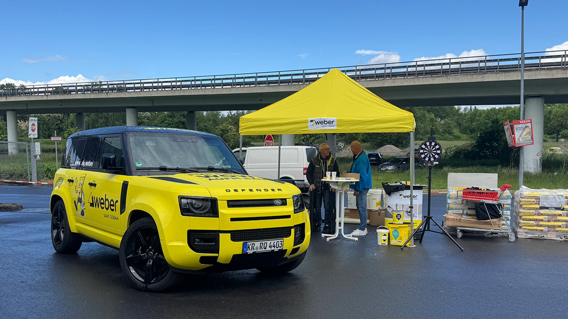 gelber Landrover Defender steht vor einem gelben Zeltdach, ein Stand ist aufgebaut, unter dem Zelt sind weber Produkte platziert