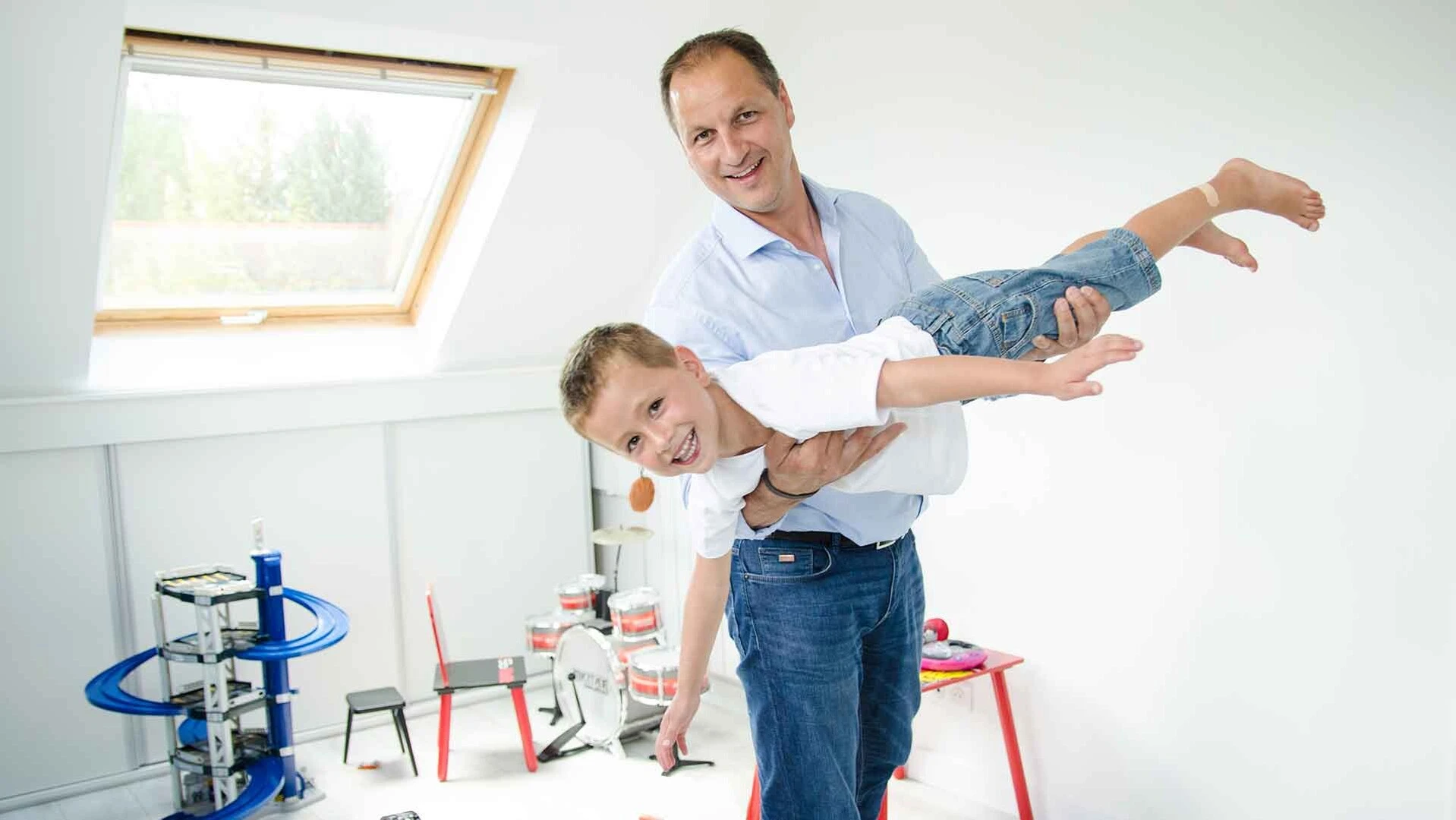 Vater und Sohn spielen in einem hellen Dachgeschosszimmer Flugzeug 