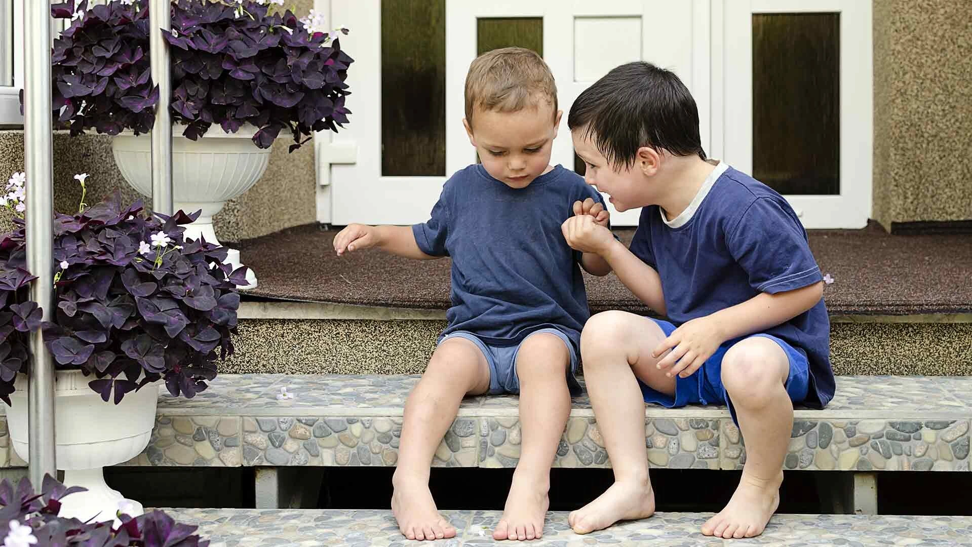 Zwei Jungen sitzen vor der Haustür auf einer Treppe, welche mit einem Buntsteinputz gestaltet ist