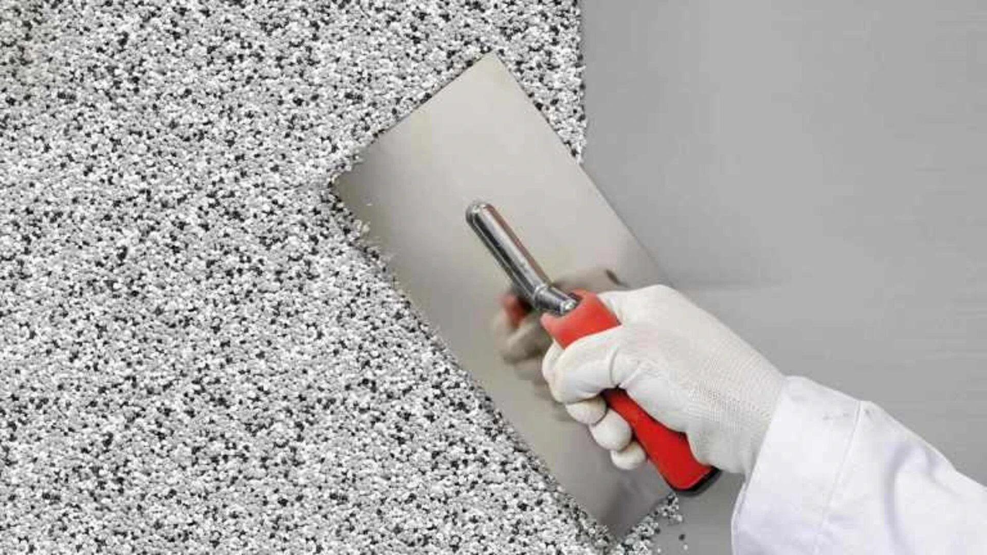 Grauer Buntsteinputz wird mit einer Kelle auf eine Wand aufgebracht