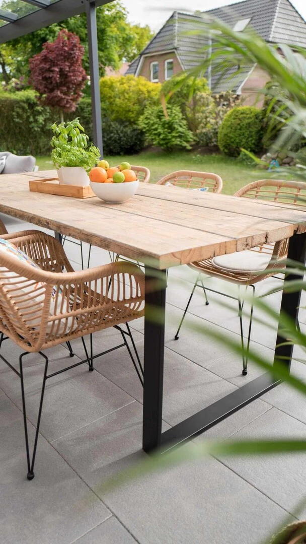 Überdachte Terrasse mit großformatigen Fliesen, Holzmöbeln und Blick in einen grünen Garten