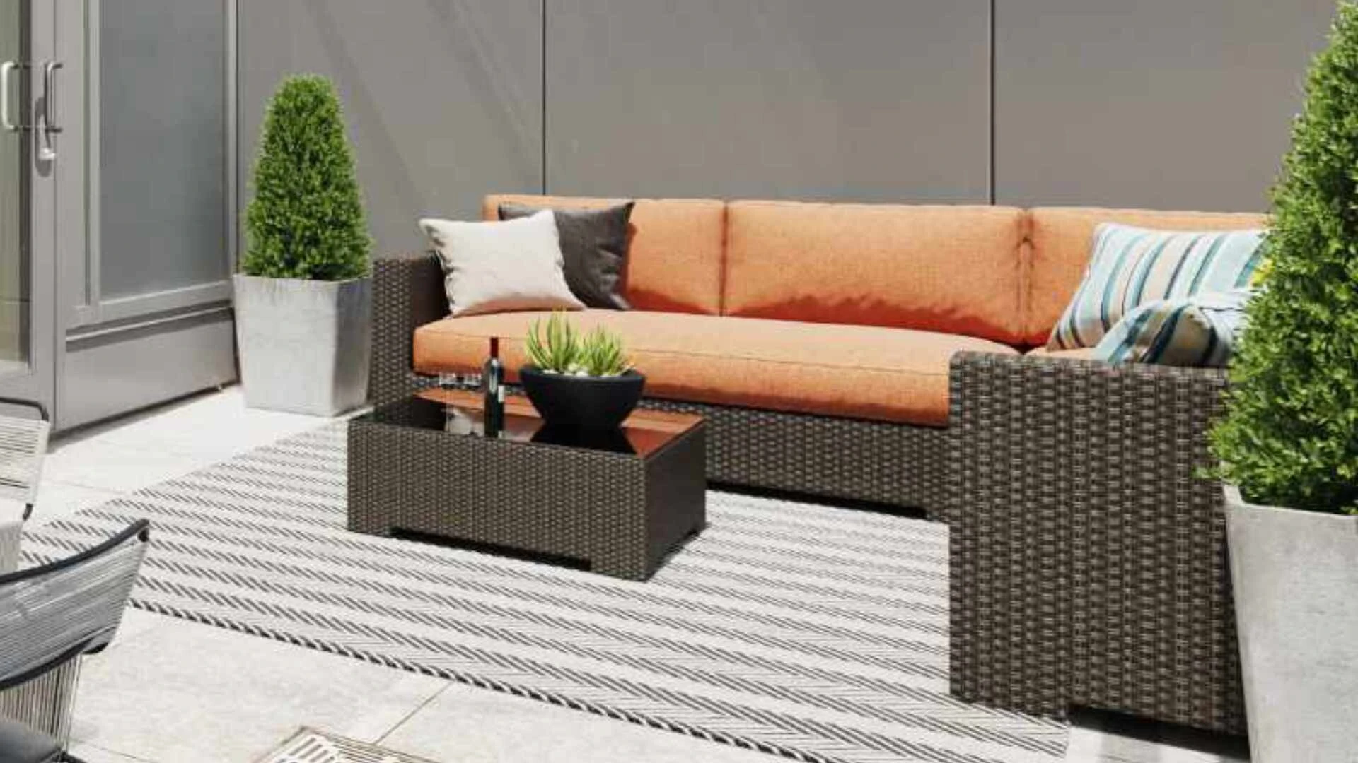 Eckaufnahme einer Terrasse mit grauen Korbmöbeln, gefliestem Boden und einer grau gefliesten Wand