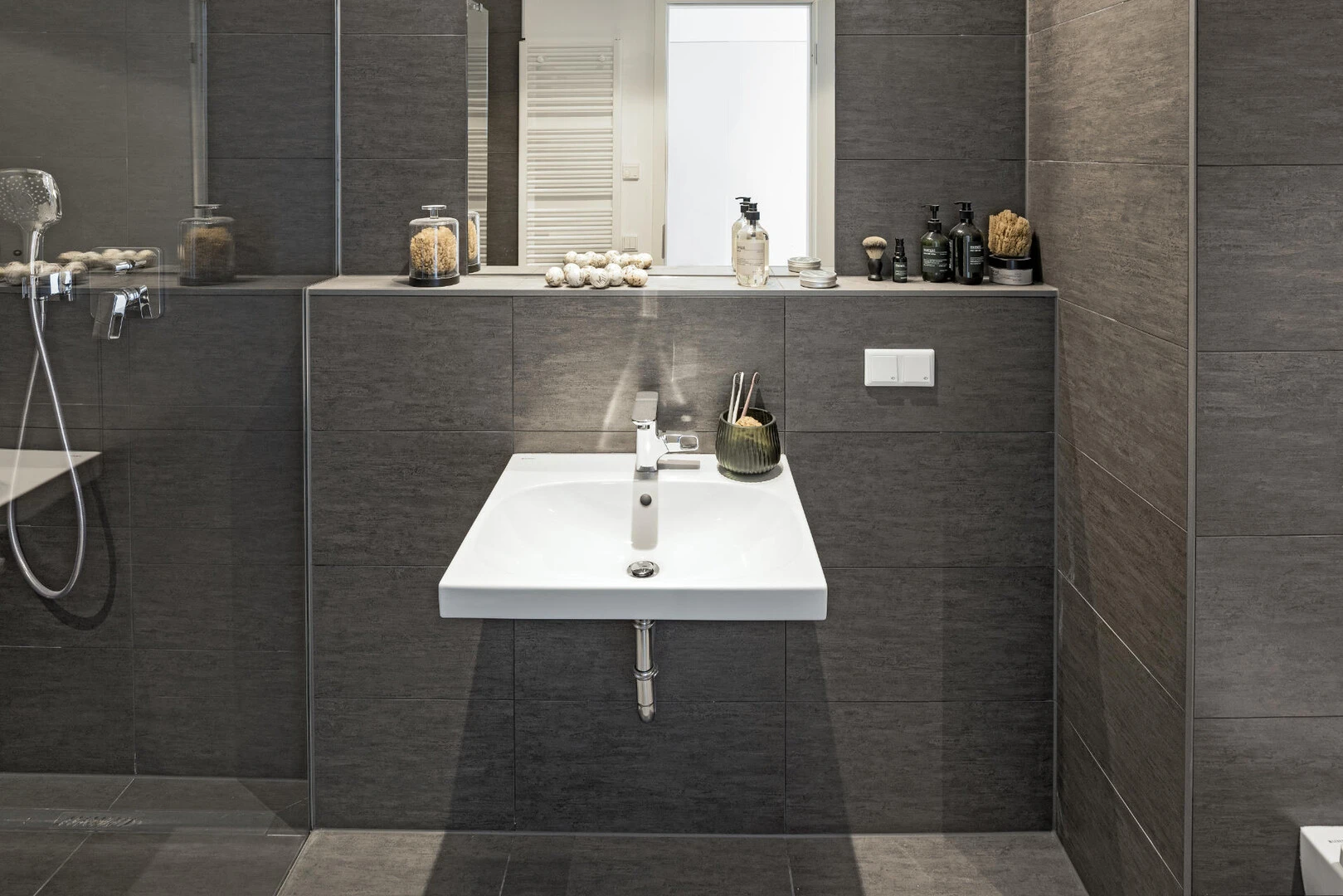 Badezimmer mit dunklen Fliesen, bodengleicher Dusche und weißem Waschbecken