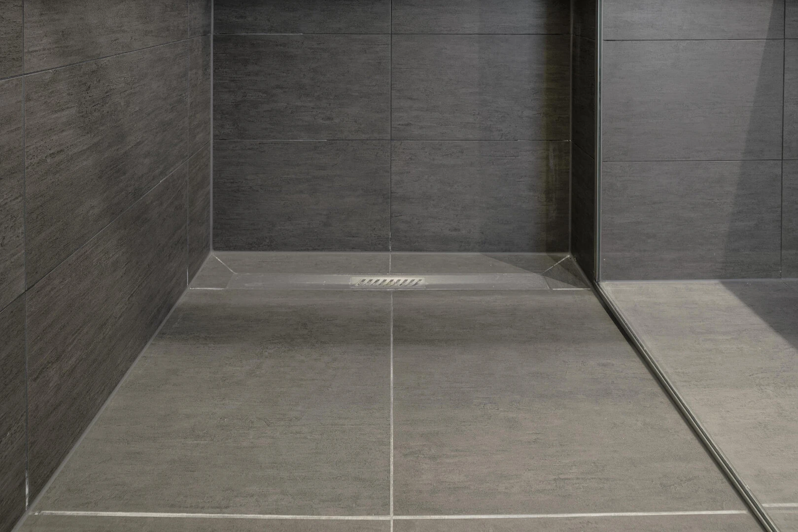 Detailaufnahme einer bodengleichen Dusche mit dunklen Fliesen