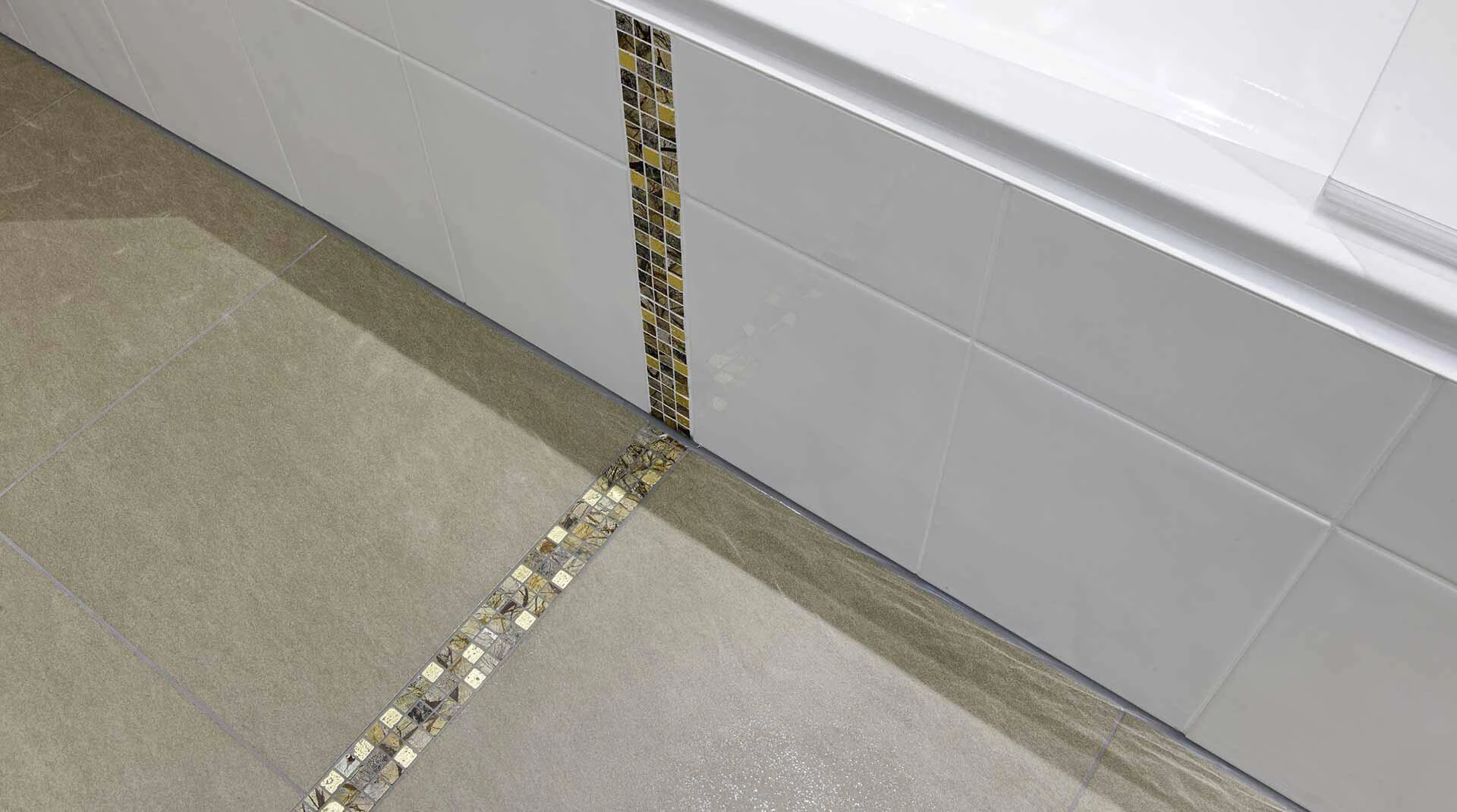 Mosaik wird als Highlight an einer gefliesten Badewanne und zwischen großformatigen Fliesen am Boden eingesetzt