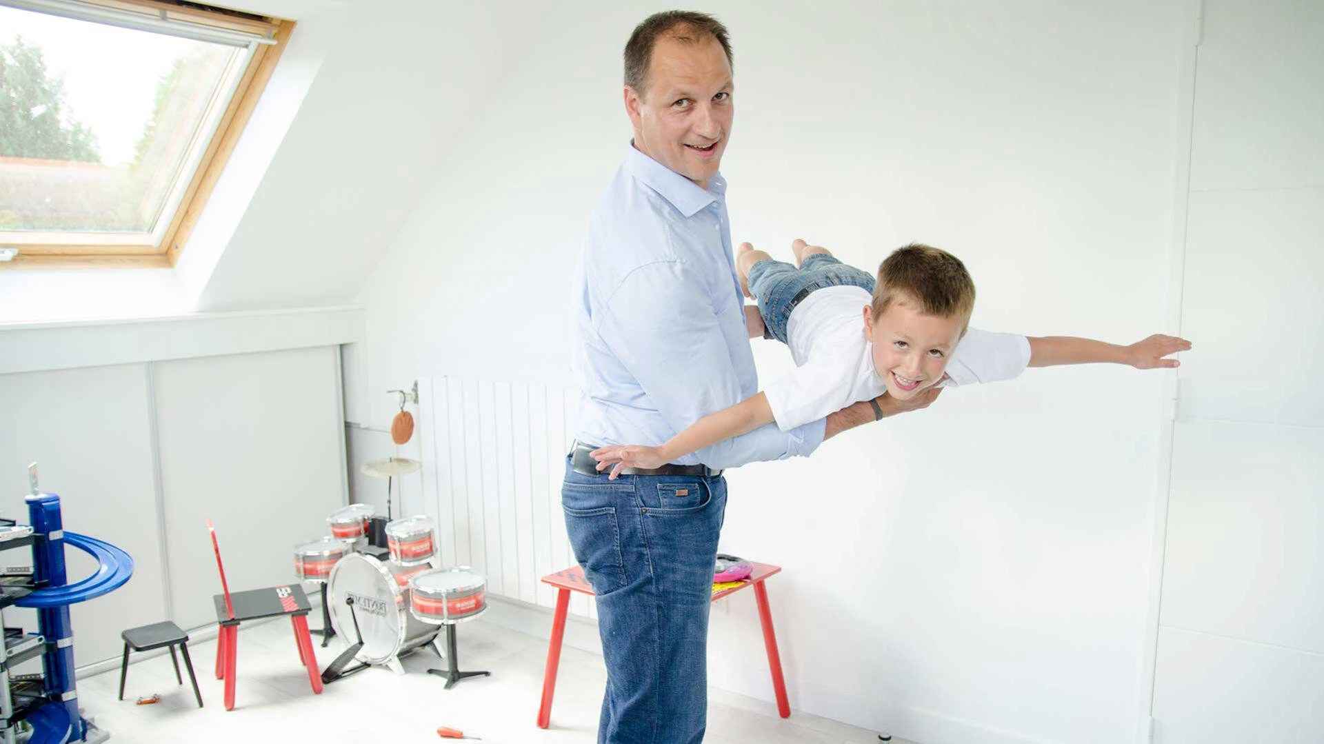 Vater hat Sohn auf dem Arm und hebt ihn wie ein Flugzeug im Kinderzimmer hoch