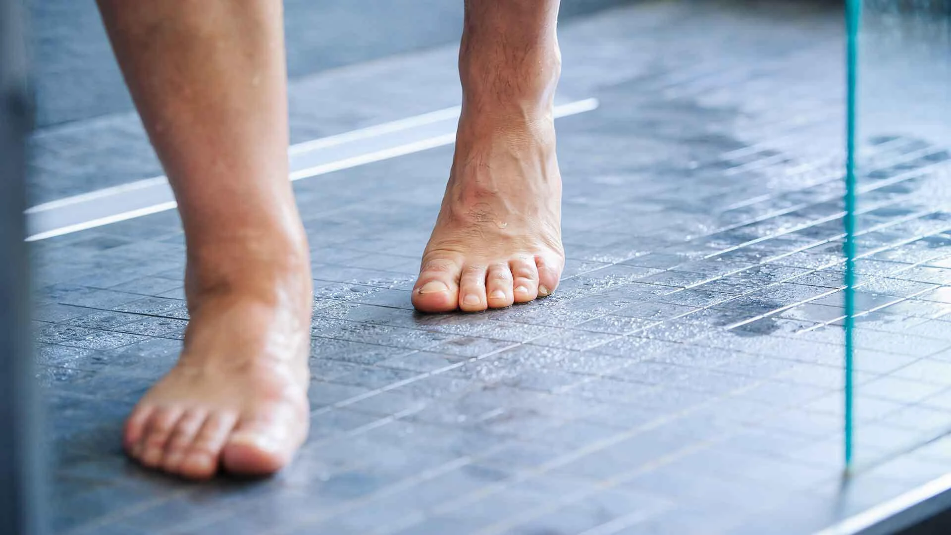 Nackte Füße laufen über einen dunkel gefliesten, feuchten Duschboden