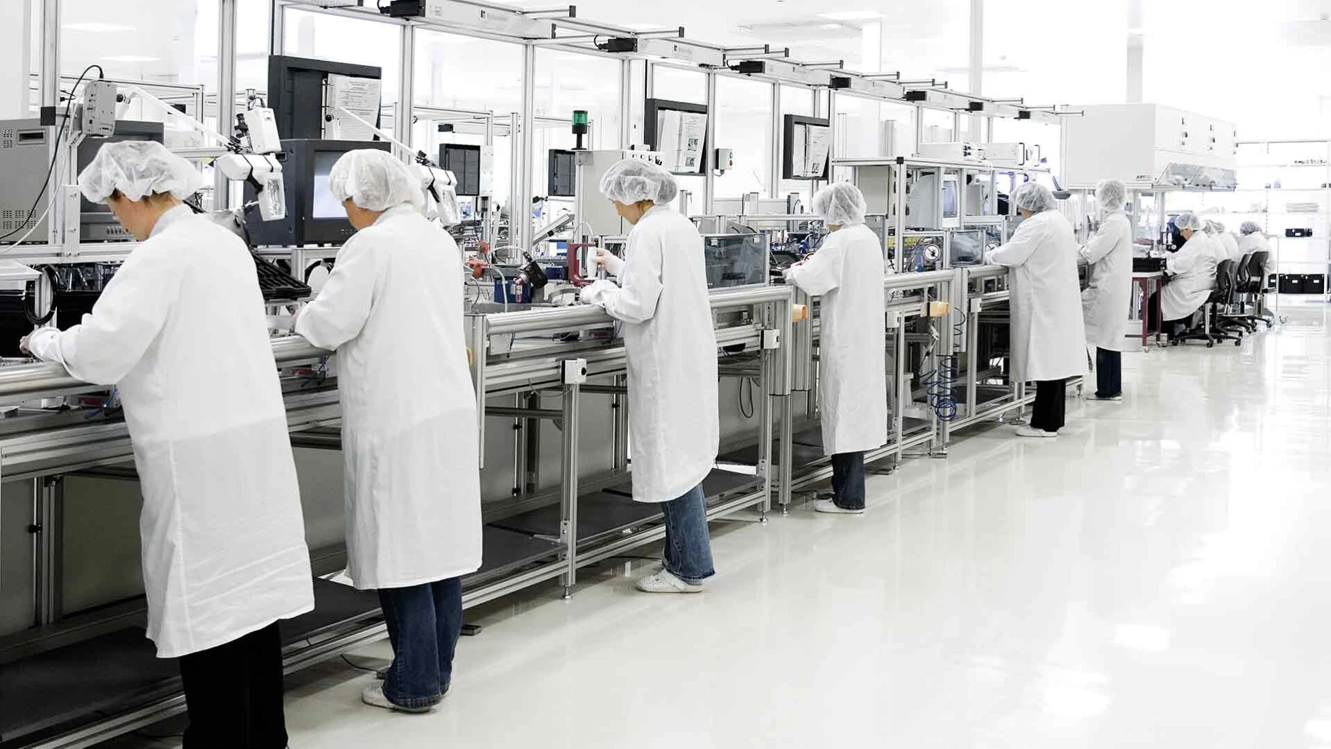 Verschiedene Personen in Schutzkleidung stehen an einer Produktionslinie in einer Produktionshalle mit Industrieboden