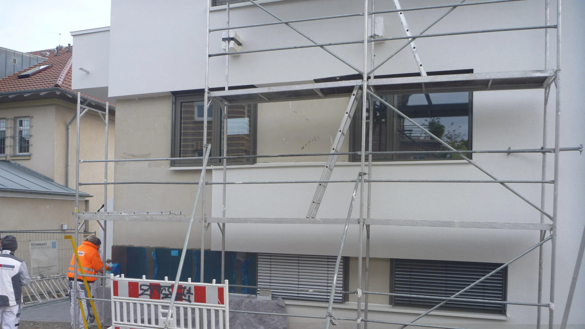 Fassade eines Mehrfamilienhauses mit Gerüst, wo Arbeiter Folie von an der Mischfassade befestigten Glasplatten abziehen