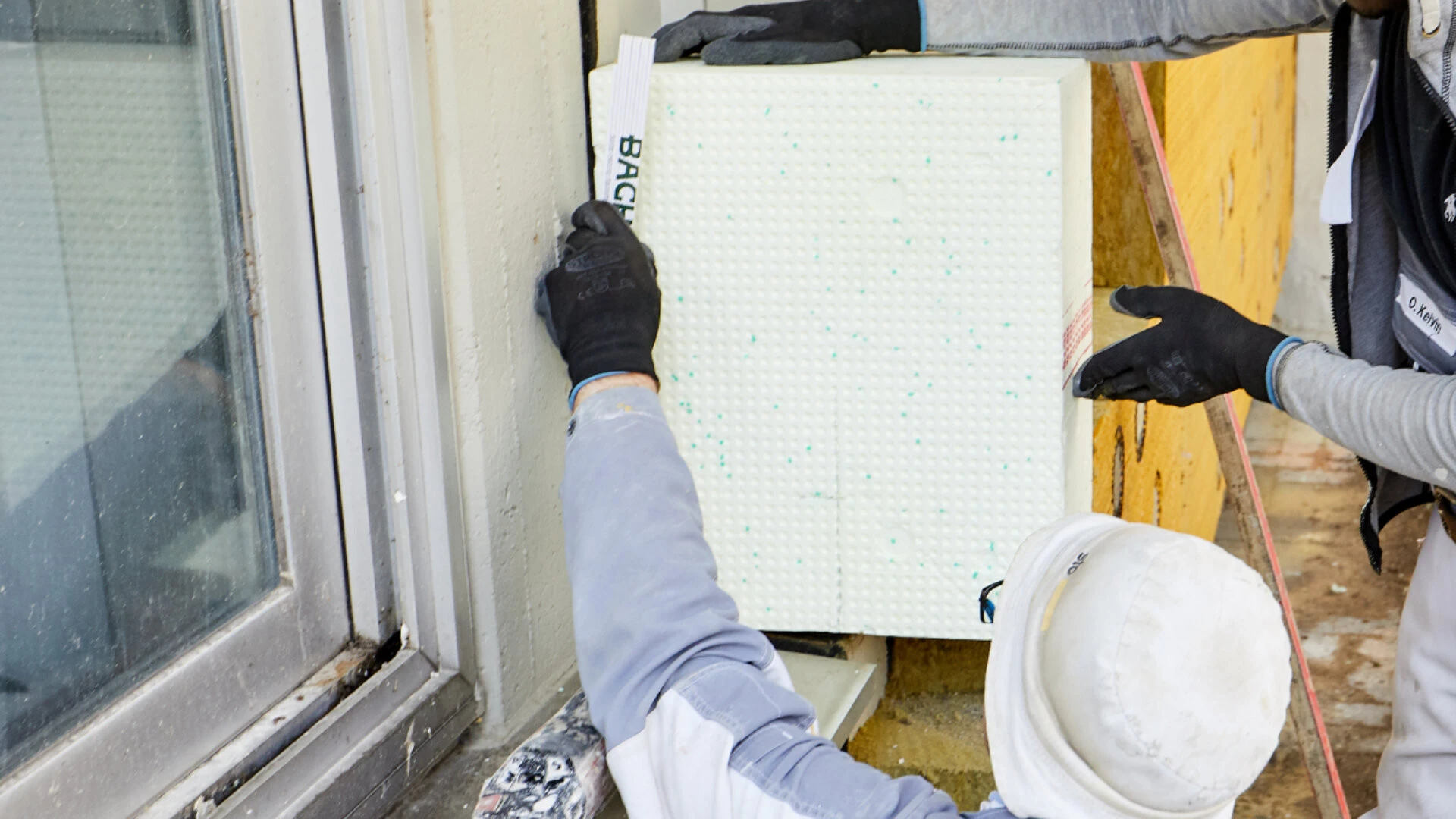 Zwei Handwerker setzen eine WDVS Dämmung an ein Fenster ein und müssen dabei Wärmebrücken vermeiden