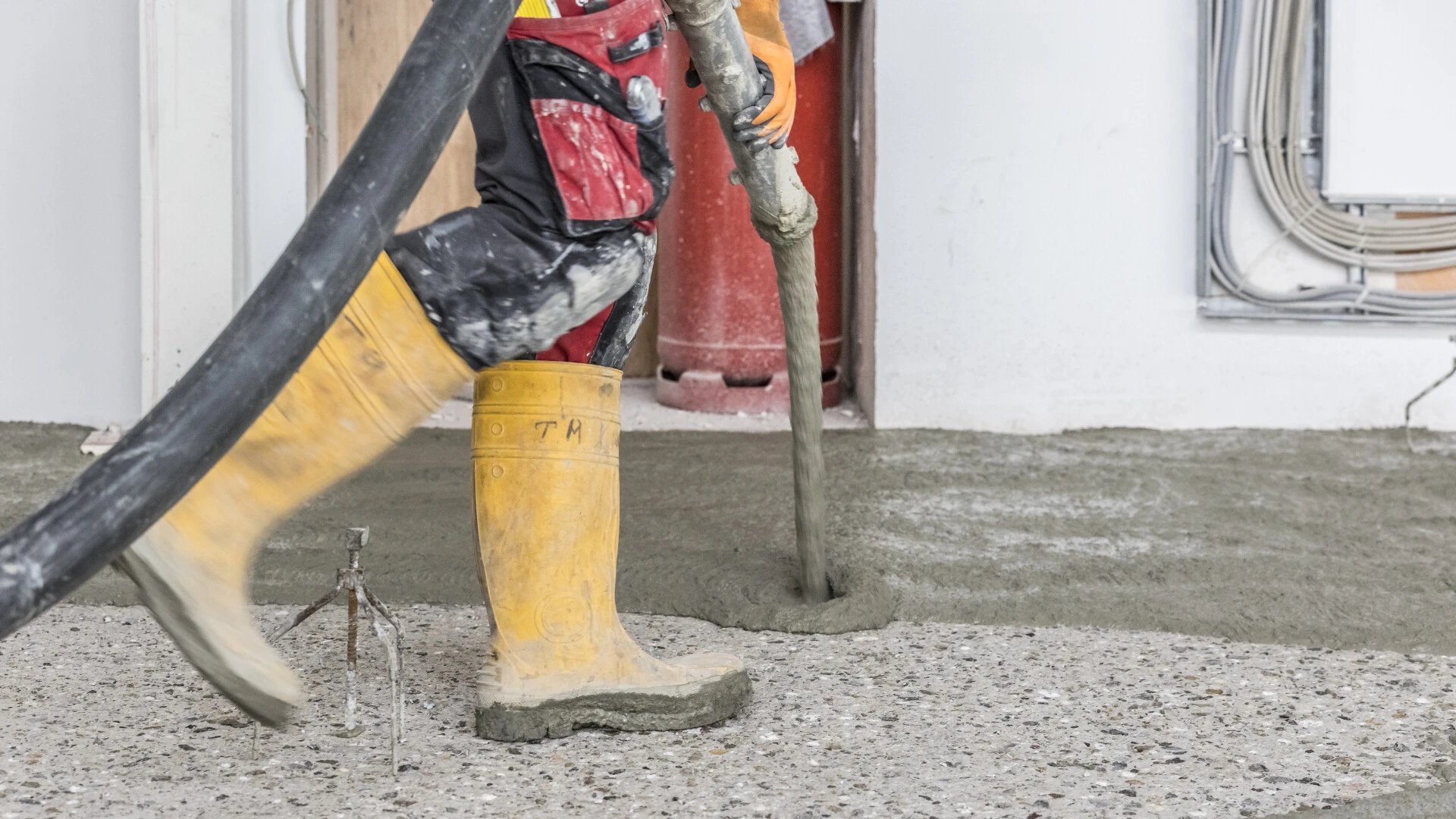 Nahaufnahme auf Stiefel und einen Schlauch, aus dem Betonersatzmörtel auf einen Betonboden gepumpt wird