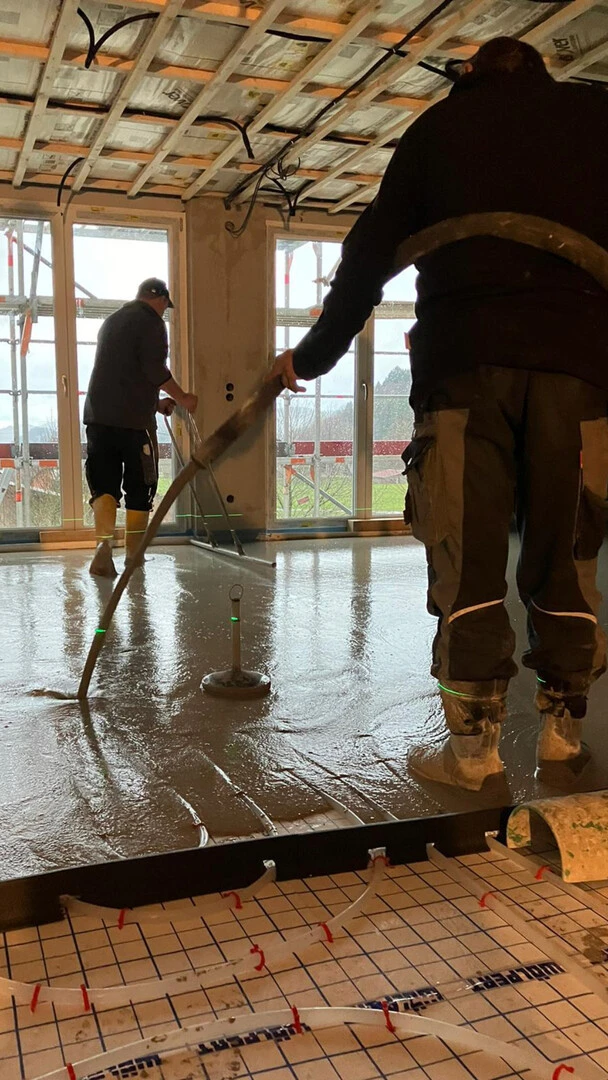 Zwei Fachhandwerker pumpen Estrich auf eine Fußbodenheizung