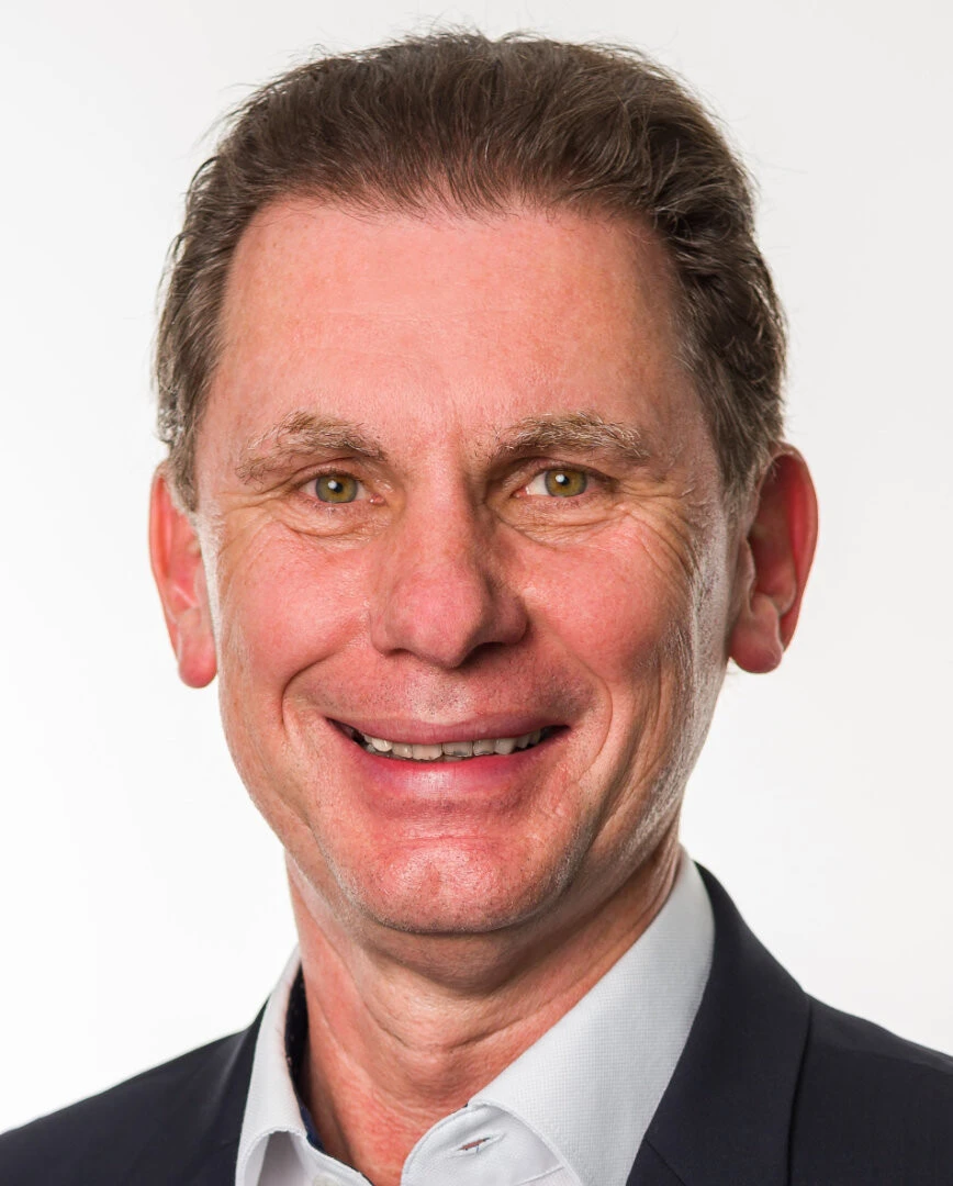 Headshot eines Mannes mit weißem Hemd und schwarzem Blazer sowie dunkelbraunen, kurzen Haaren