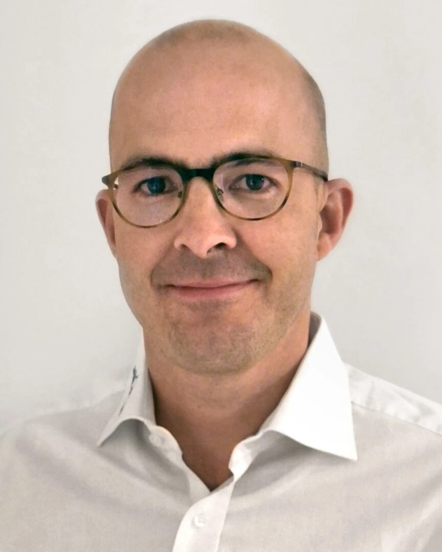 Headshot eines jungen Manns mit weißem Hemd, Glatze und Brille
