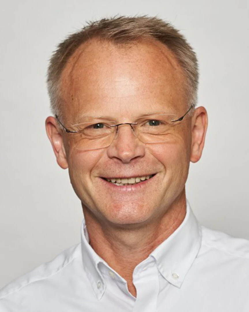 Headshot eines Mannes mit weißem Hemd, rahmenloser Brille und kurzen, grauen Haaren