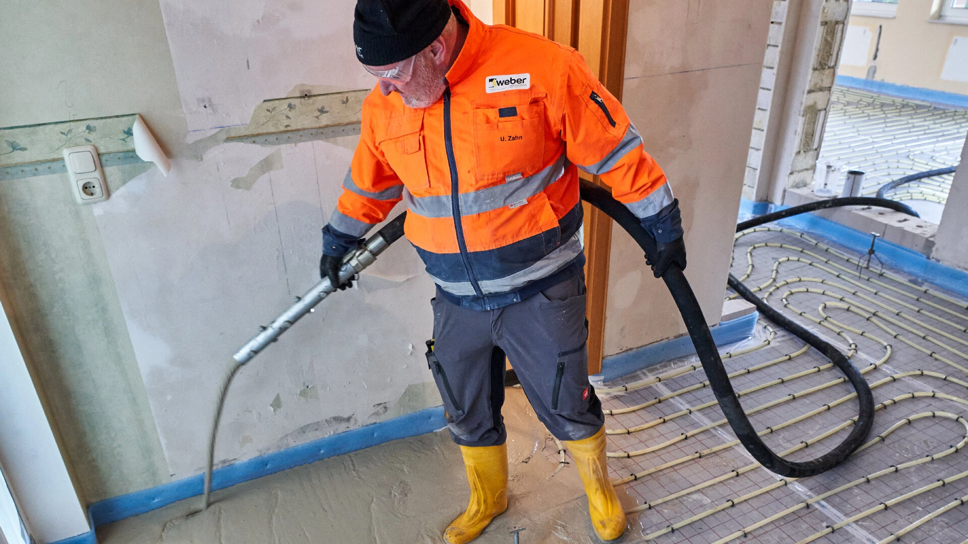 Aufnahme eines Handwerkers, der aus einem Schlauch Fließestrich auf eine Fußbodenheizung pumpt
