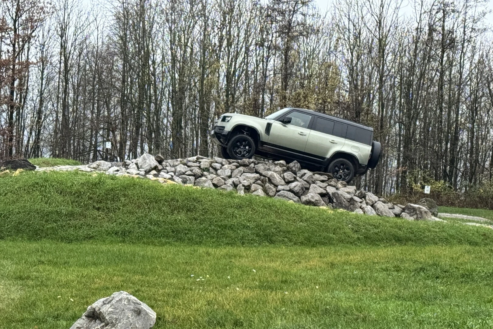 Geländewagen steht auf einem Hügel aus großen Steinen in einem Offroad-Parcours. Im Hintergrund sind kahle Bäume und eine grüne Wiese zu sehen