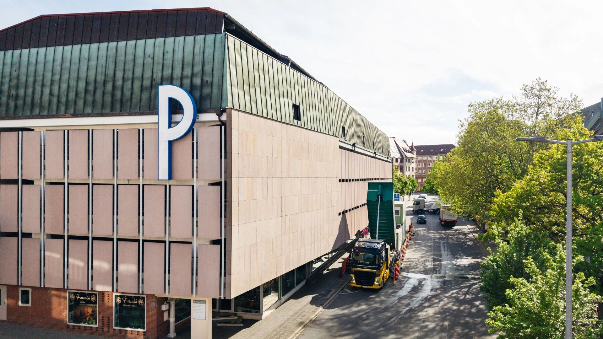 Parkhaus mit laufenden Sanierungsarbeiten an der Betonkonstruktion. Baustellenfahrzeuge und Arbeitsbereich vor dem Gebäude zeigen die laufende Instandsetzung.