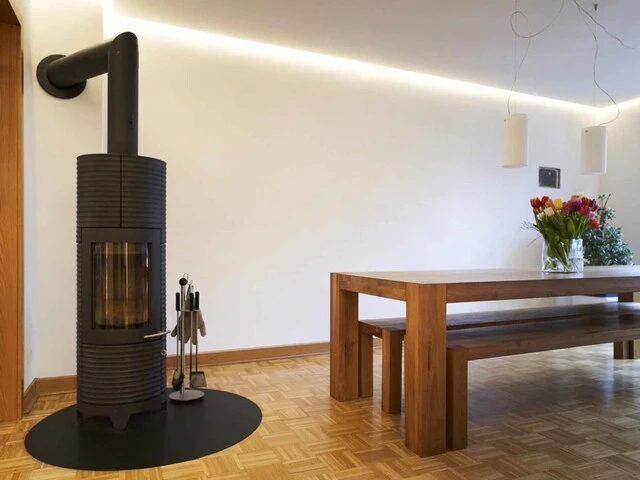 Wohnzimmer mit Holzboden, schwarzem Kamin, Holztisch und weißen, mit Kalkputz verputzten Wänden