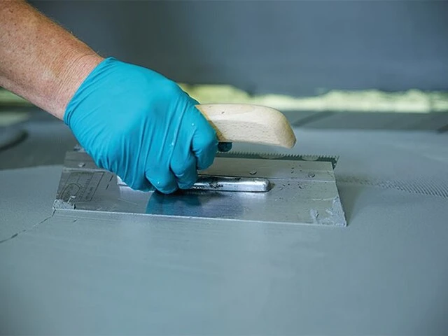 Gefälleestrich abdichten: flexible Dichtungsschlämme wird mit Spachtel am Boden glatt gezogen