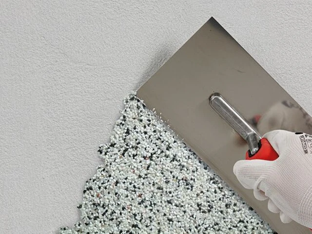 Buntsteinputz wird mit einer Putzkelle an der Wand angebracht