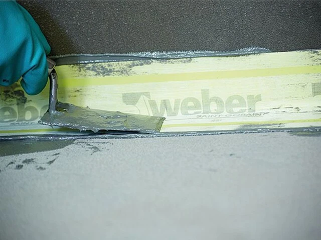 Gefälleestrich abdichten: Dichtband wird mit Spachtel in Dichtungsschlämme eingebettet
