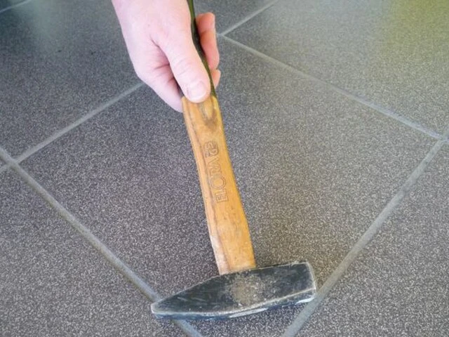 Fliesenboden wird vorsichtig mit einem Hammer abgeklopft